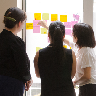 Three people analyzing sticky notes on the wall at a workshop